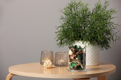Glass jar with aromatic potpourri of dried flowers and beautiful houseplant on wooden table indoors. Space for text