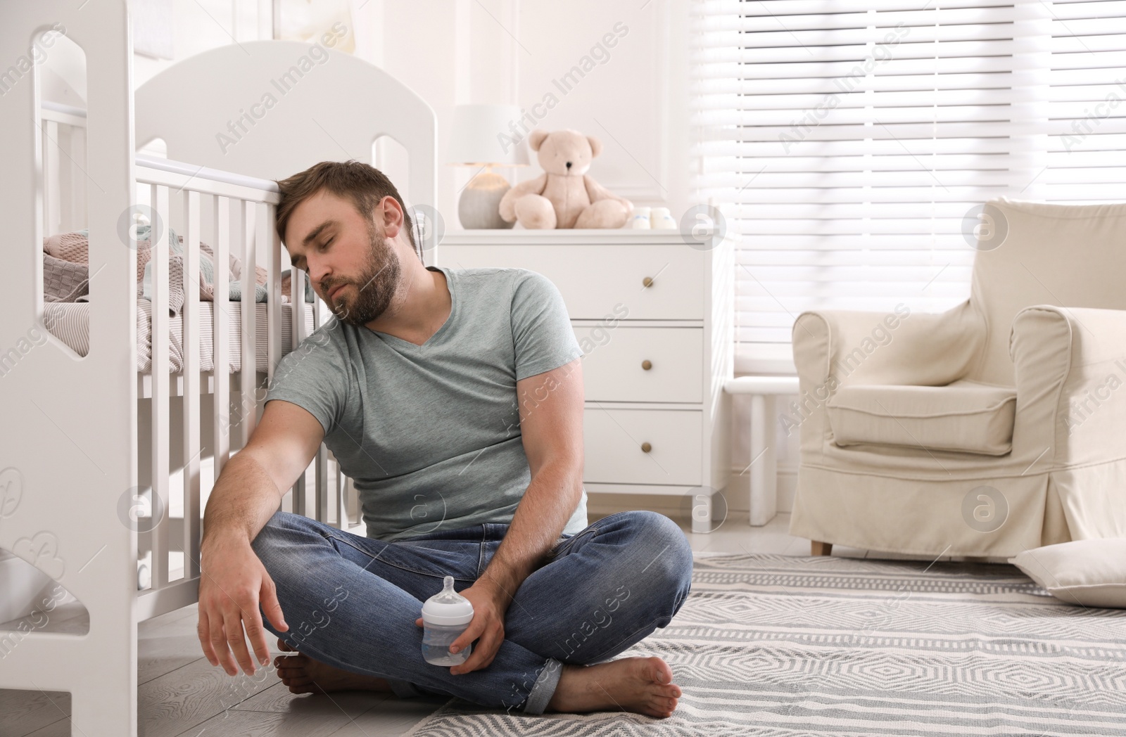 Photo of Tired father with bottle of milk sleeping on floor in children's room