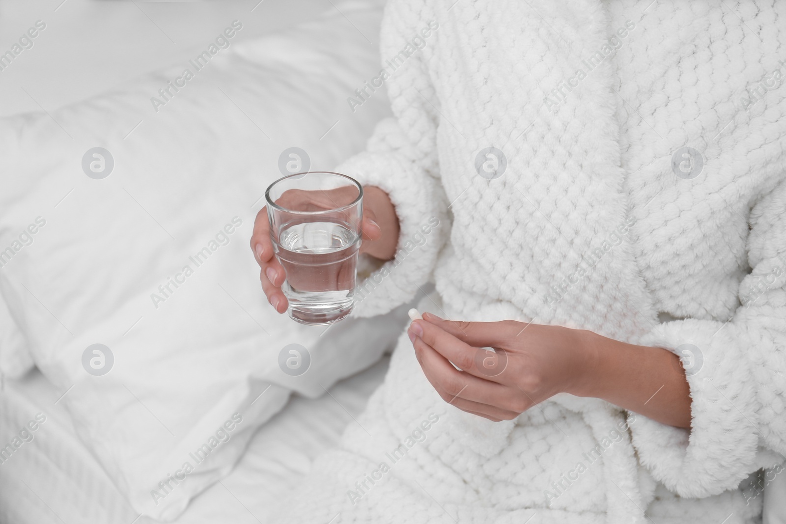 Photo of Young woman with glass of water taking pill in bedroom, closeup