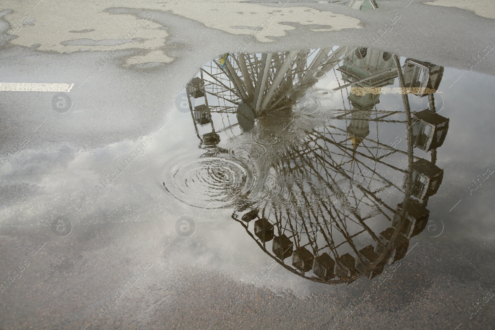 Photo of Reflection of Ferris wheel in puddle on asphalt outdoors