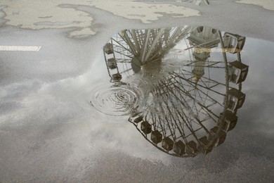 Photo of Reflection of Ferris wheel in puddle on asphalt outdoors