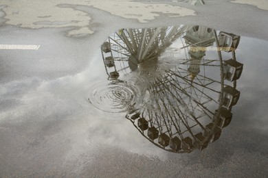 Reflection of Ferris wheel in puddle on asphalt outdoors