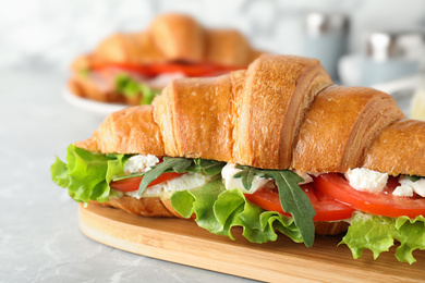 Photo of Tasty croissant sandwich with feta cheese and tomato on light grey marble table, closeup