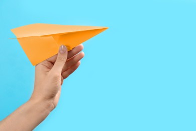 Image of Woman holding orange paper plane on light blue background, closeup. Space for text