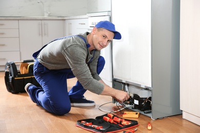 Male technician in uniform repairing refrigerator indoors