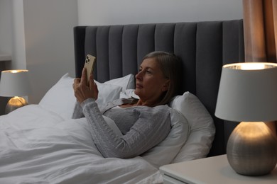 Photo of Menopause. Sleepless woman using smartphone in bed indoors