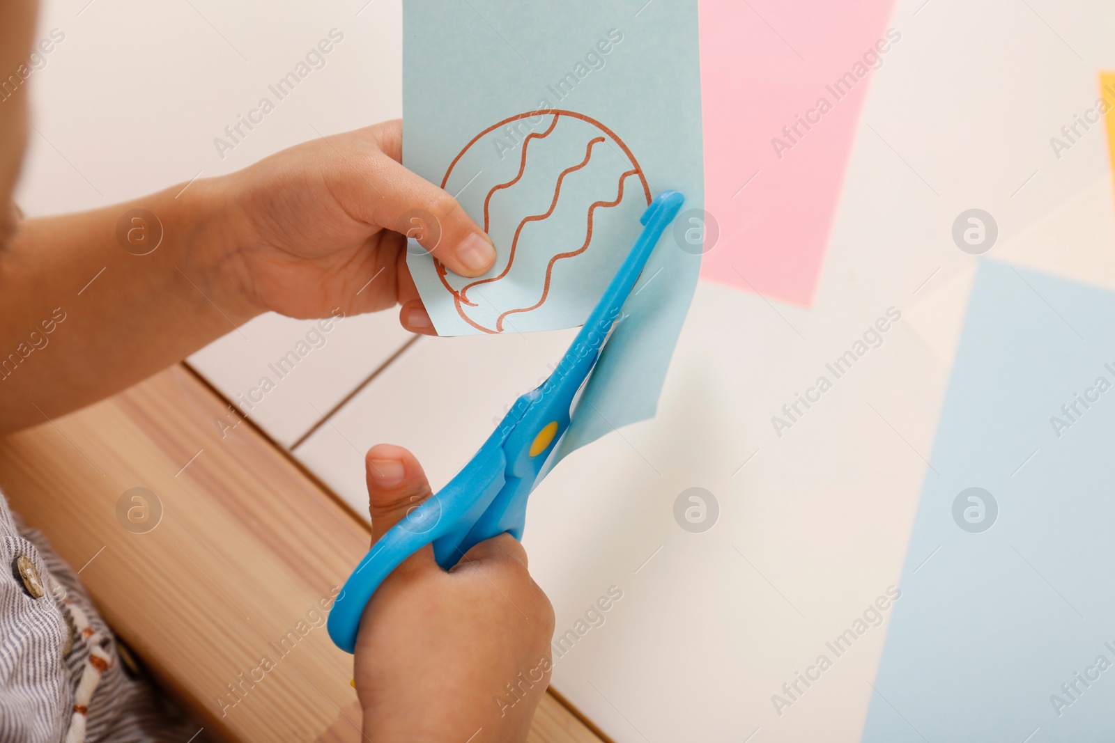 Photo of Little girl cutting color paper with scissors at table, closeup