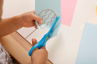 Photo of Little girl cutting color paper with scissors at table, closeup