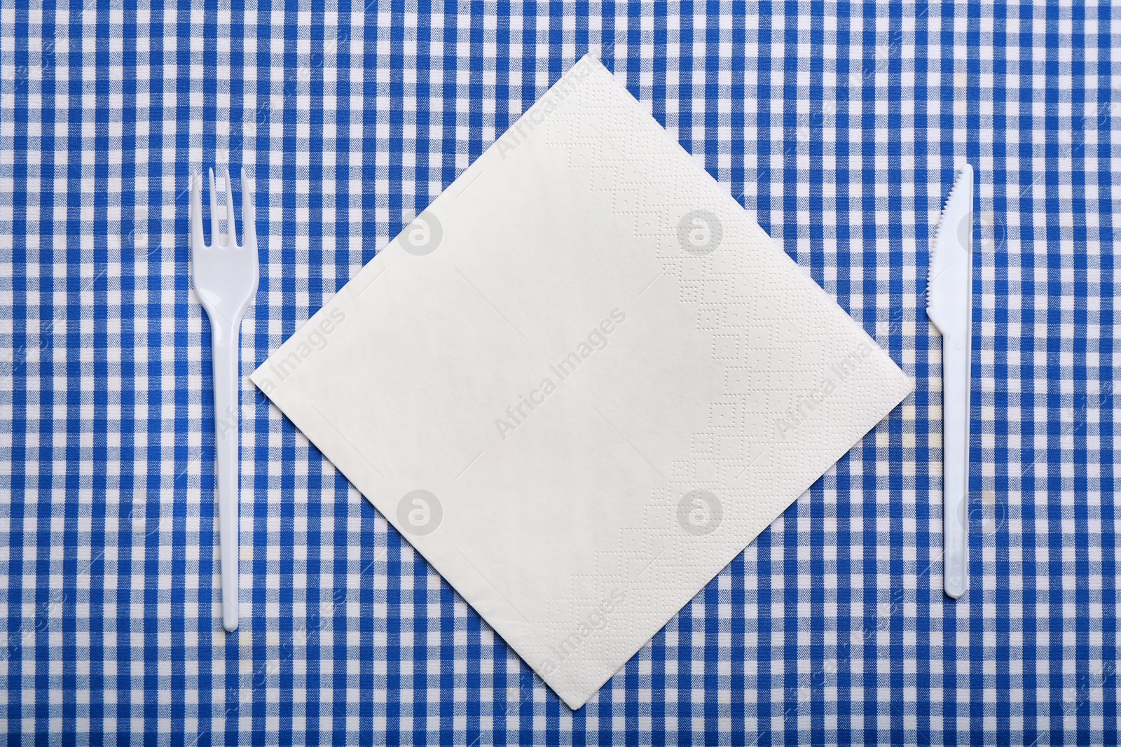 Photo of Plastic cutlery and napkin with space for text on plaid fabric, flat lay. Table setting