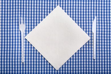 Plastic cutlery and napkin with space for text on plaid fabric, flat lay. Table setting