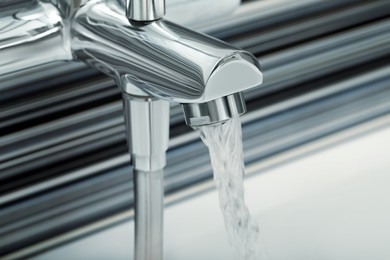 Photo of Water flowing from bath tap on blurred background, closeup