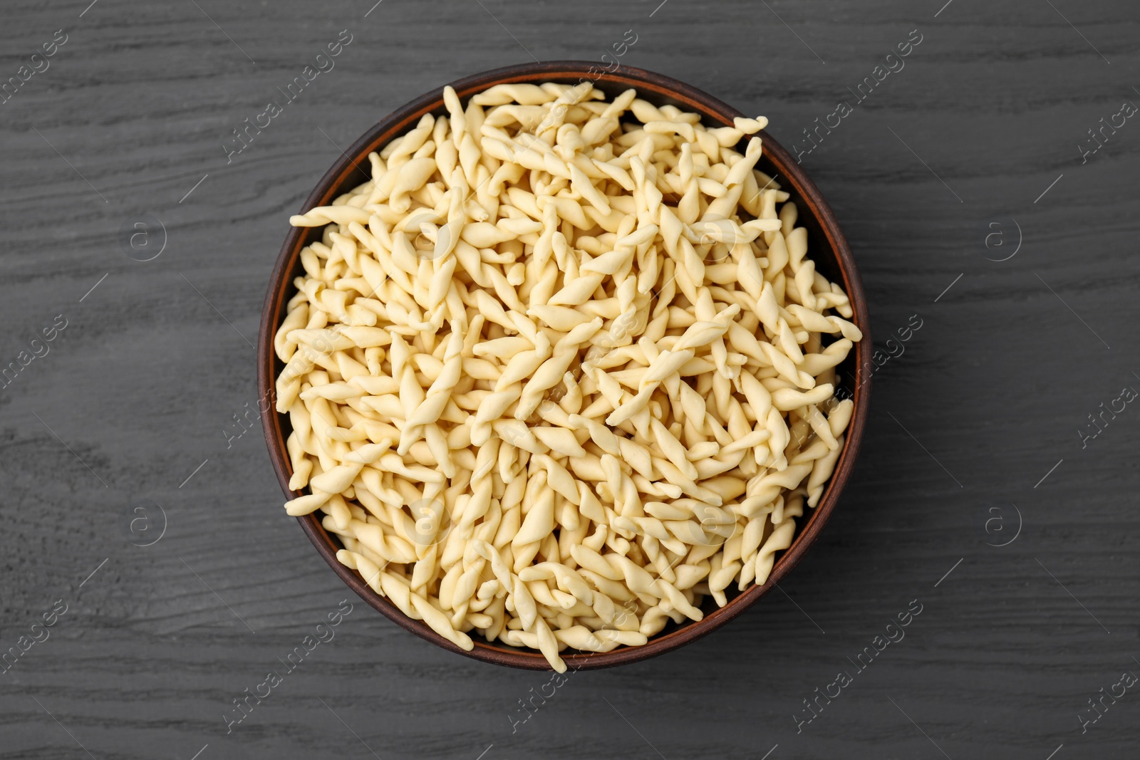 Photo of Uncooked trofie pasta in bowl on grey wooden table, top view