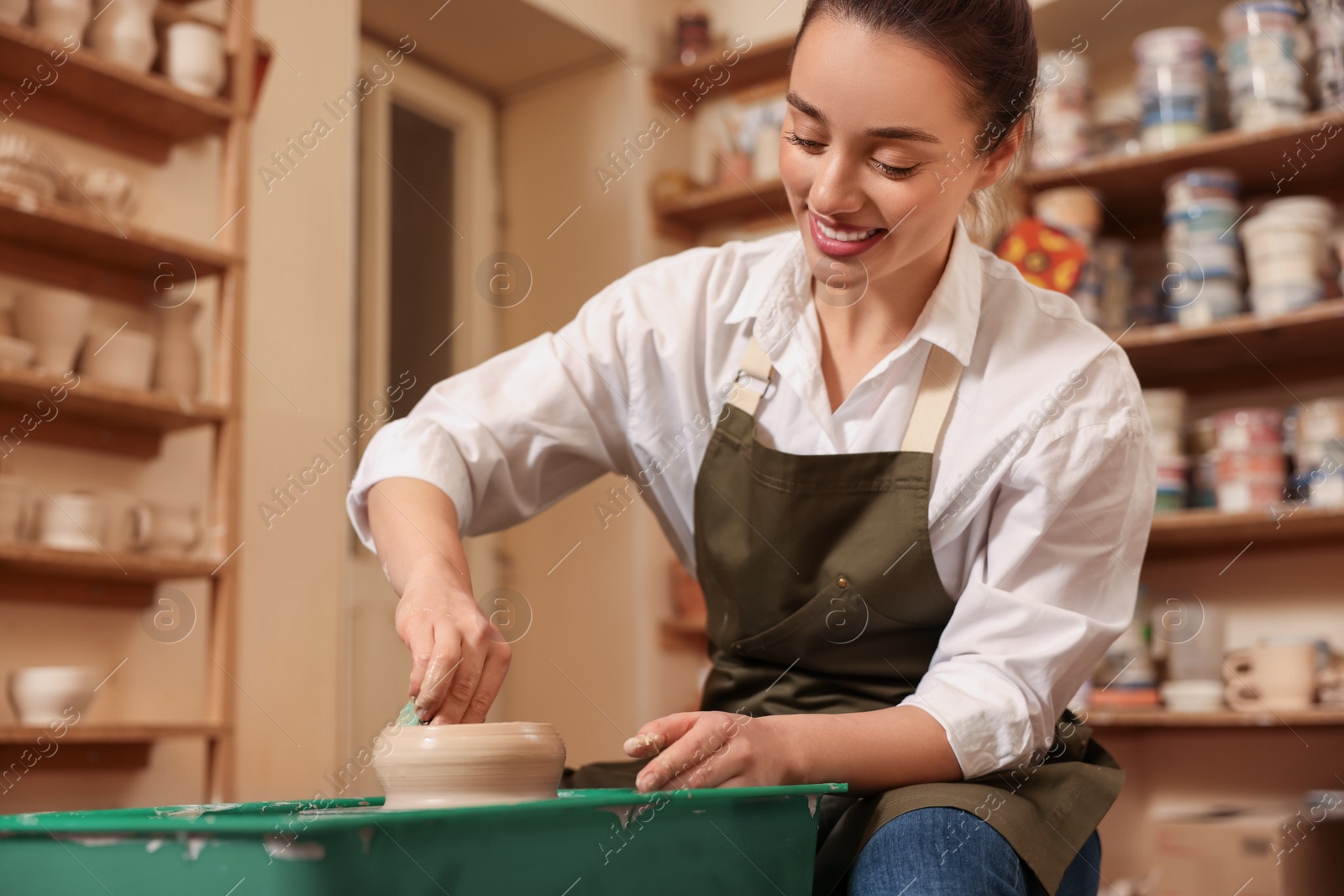 Photo of Clay crafting. Smiling woman making bowl on potter's wheel in workshop