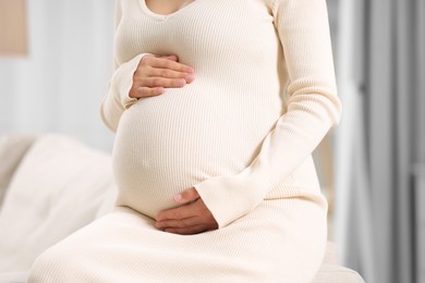 Photo of Pregnant woman in white dress indoors, closeup