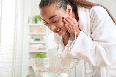 Photo of Beautiful young woman washing her face with water in bathroom