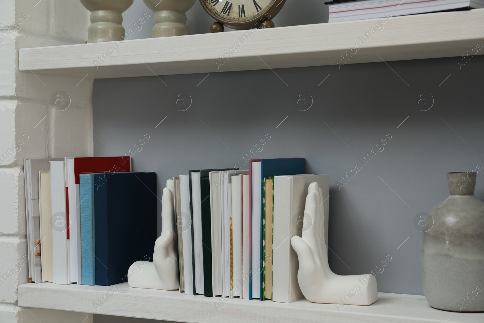 Photo of Hand shaped bookends with books on shelf indoors. Interior design