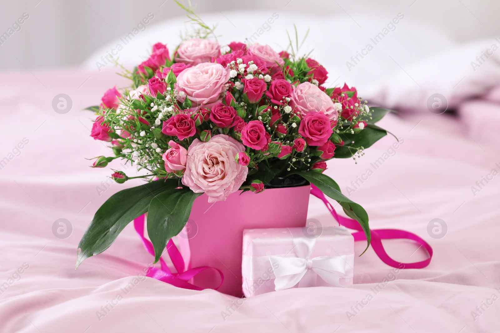 Photo of Beautiful bouquet of flowers and gift box on bed