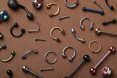 Photo of Stylish piercing jewelry on brown background, flat lay