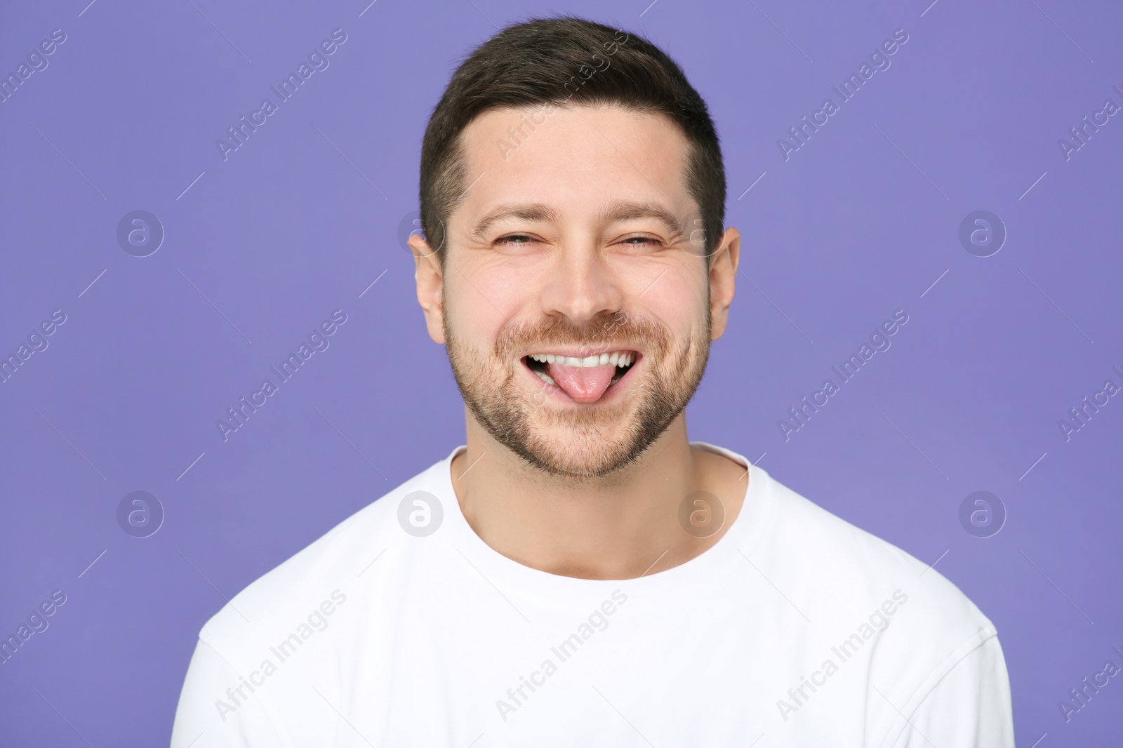 Photo of Happy man showing his tongue on purple background