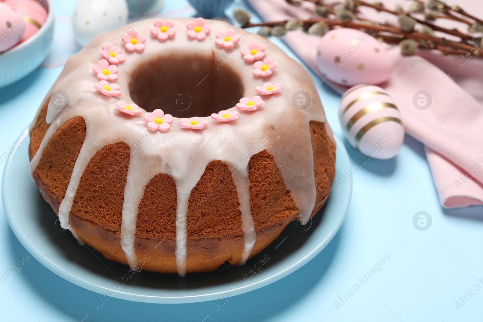 Photo of Delicious Easter cake decorated with sprinkles near painted eggs on light blue background, closeup