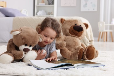 Photo of Cute little girl reading book near teddy bears on floor at home