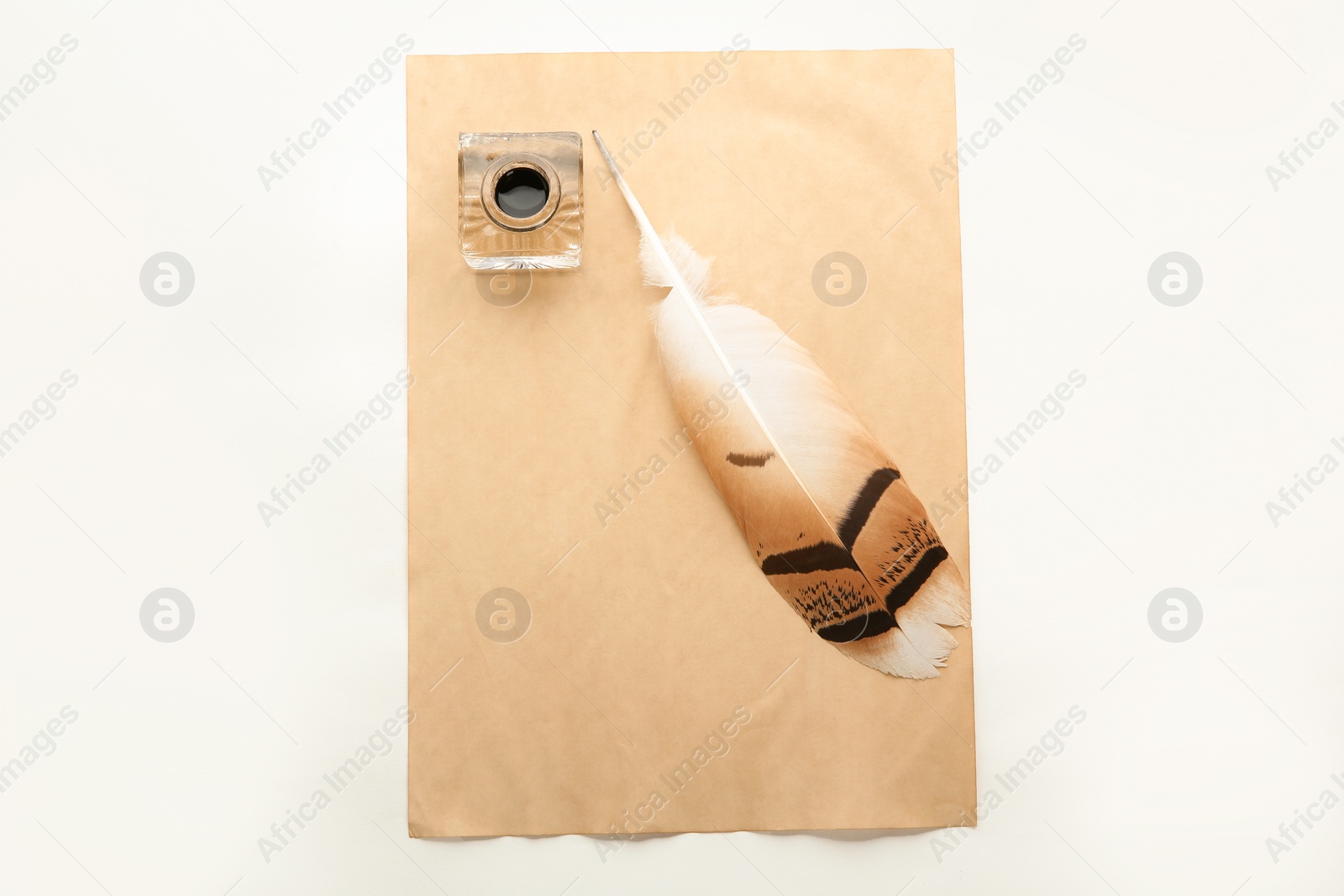 Photo of Feather pen, inkwell and sheet of paper on white background, top view. Space for text