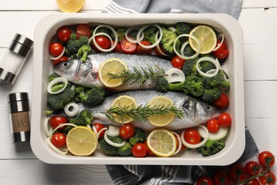 Photo of Raw fish with vegetables in baking dish and lemon on white wooden table, flat lay