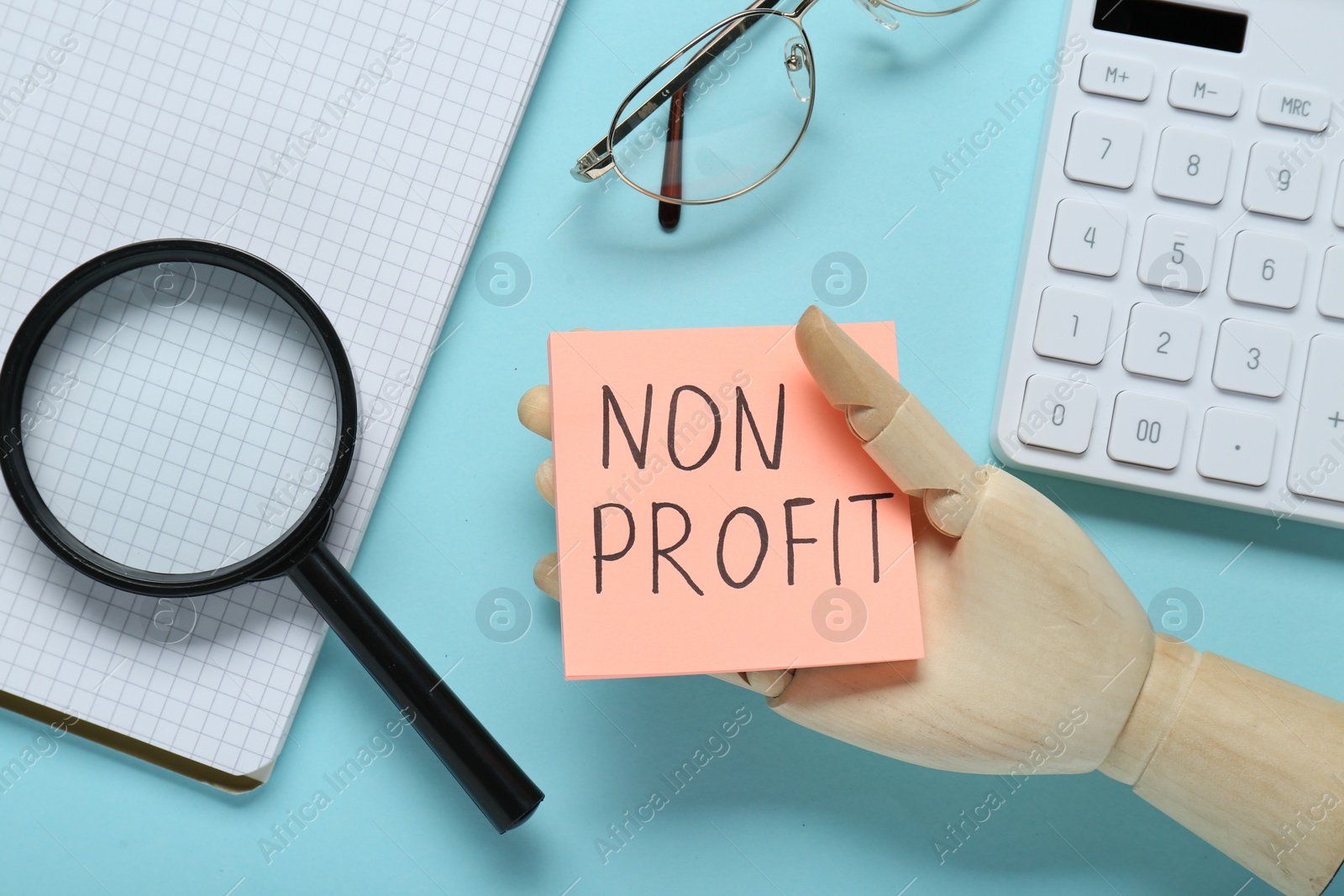 Photo of Non Profit concept. Flat lay composition with paper note in wooden mannequin hand on light blue background