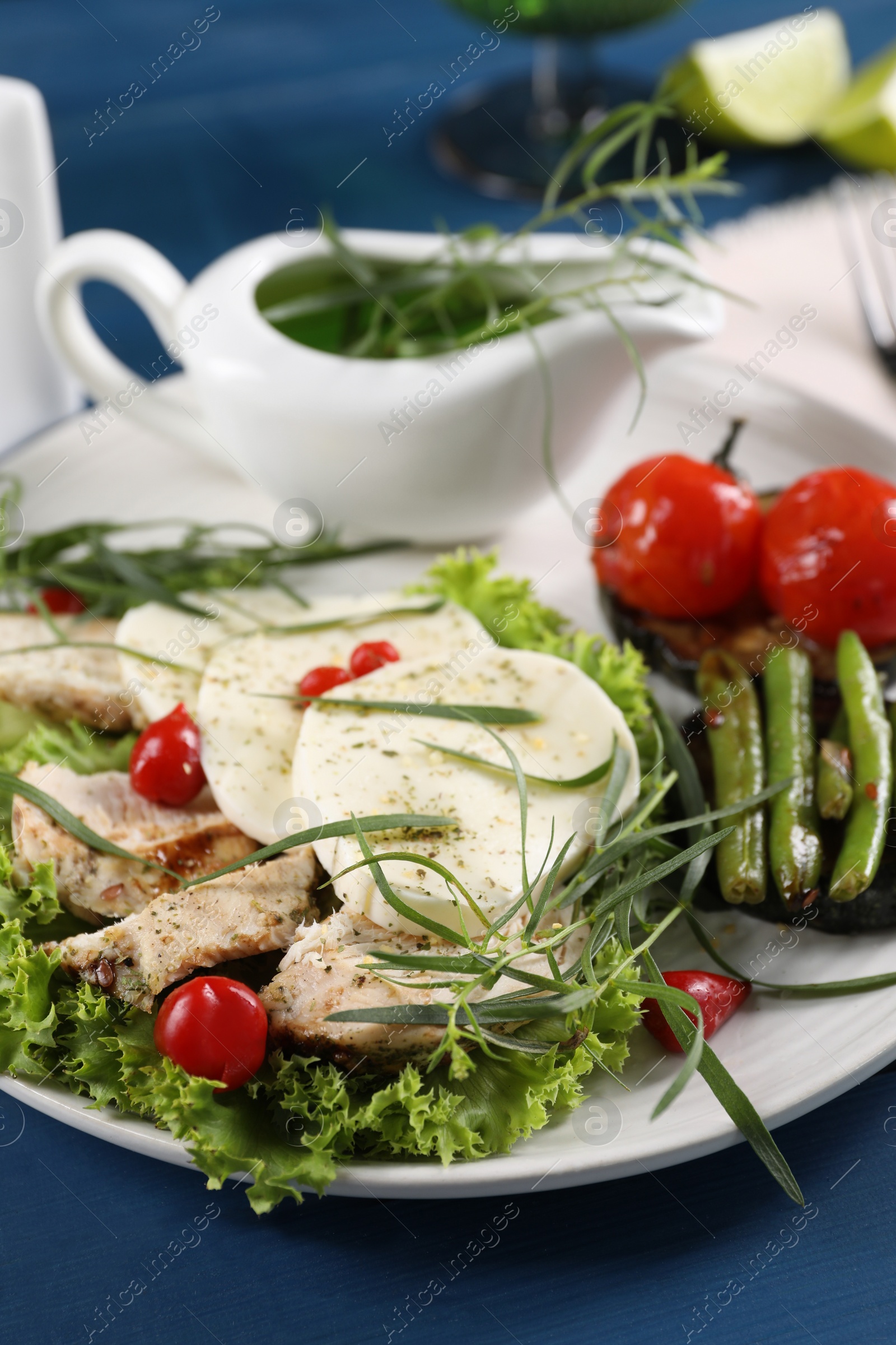 Photo of Tasty mozzarella, chicken and vegetables with tarragon on blue wooden table, closeup