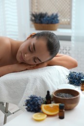 Photo of Beautiful young woman relaxing on massage couch and bottles of essential oil with ingredients on table in spa salon
