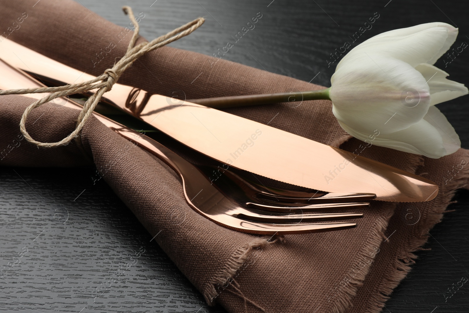 Photo of Stylish setting with cutlery, flower and napkin on black wooden table, closeup