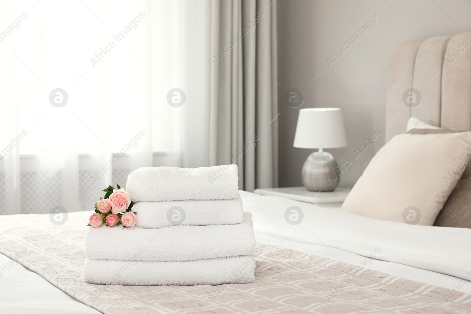 Photo of Stack of fresh towels with flowers on bed indoors, space for text