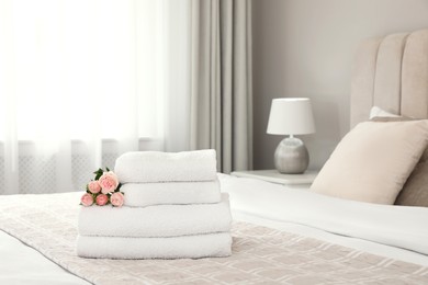 Photo of Stack of fresh towels with flowers on bed indoors, space for text