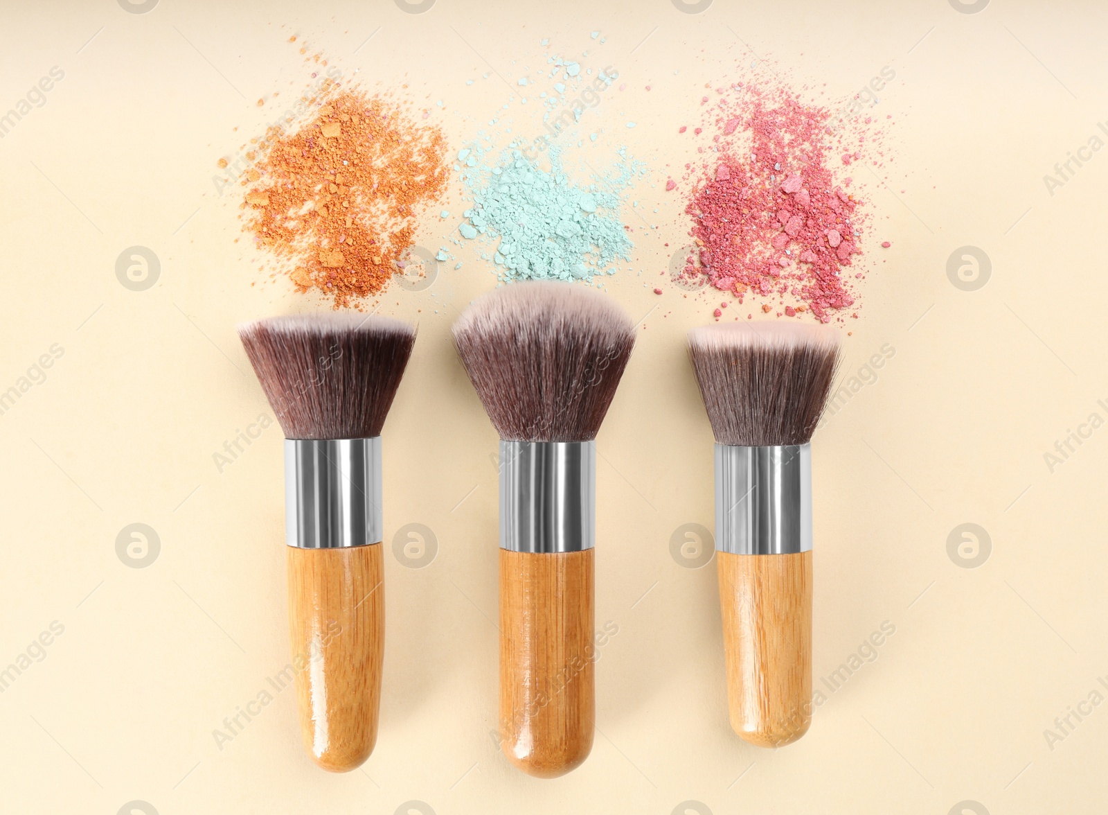 Photo of Makeup brushes and scattered eye shadows on beige background, flat lay