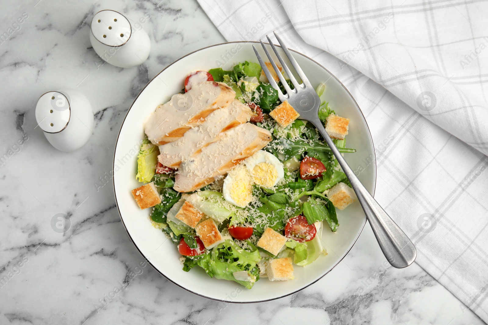 Photo of Delicious Caesar salad in bowl on white marble table, flat lay