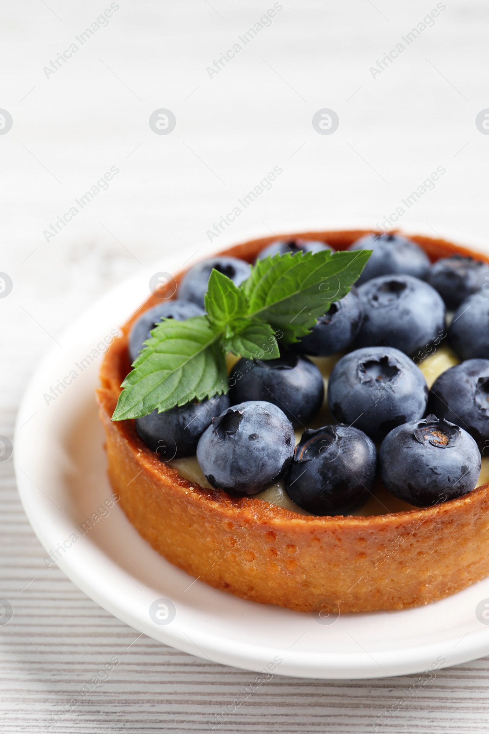 Photo of Tartlet with fresh blueberries on white wooden table, closeup. Delicious dessert