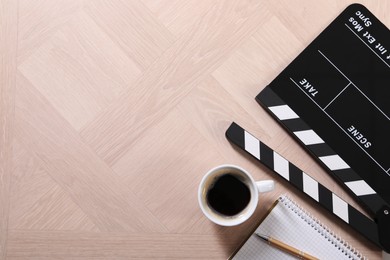 Photo of Movie clapper, coffee, notebook and pen on wooden table, flat lay. Space for text