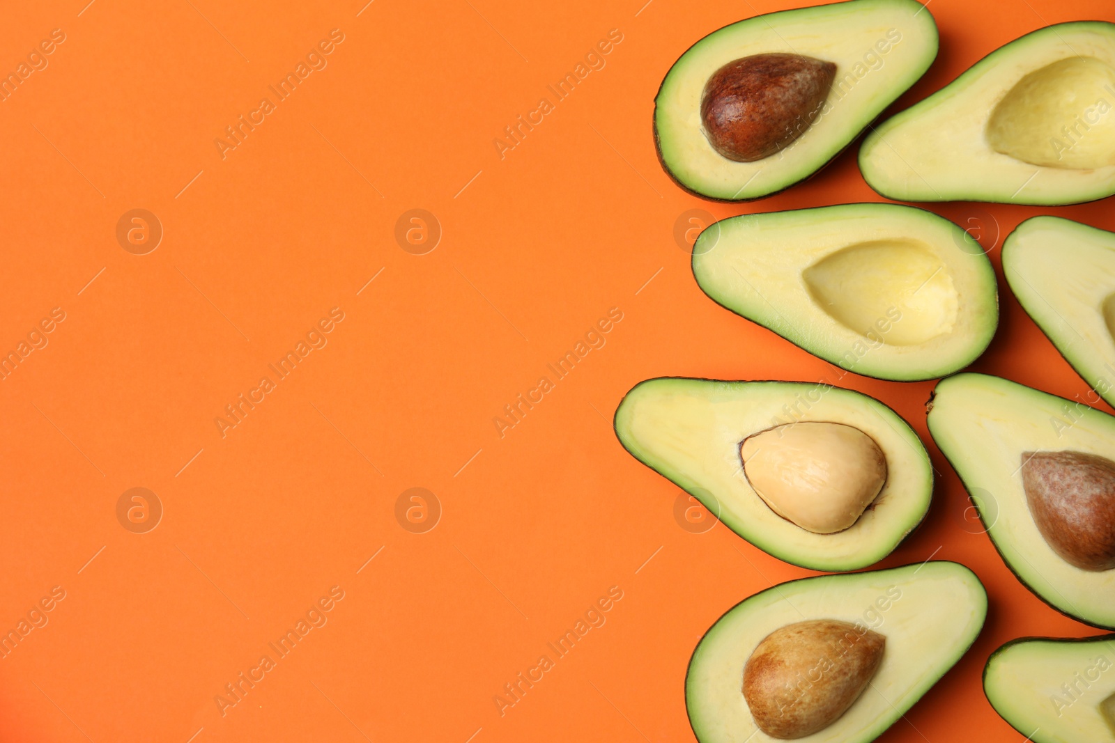 Photo of Cut fresh ripe avocados on orange background, flat lay with space for text