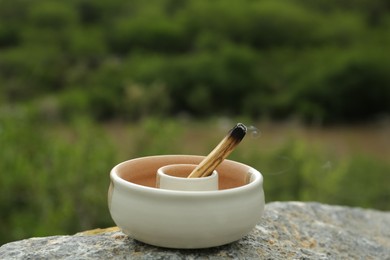 Burnt palo santo stick on stone surface outdoors, closeup