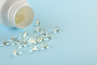 Photo of Bottle and vitamin capsules on light blue background, closeup. Space for text