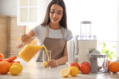Photo of Young woman pouring tasty fresh juice into glass at table in kitchen
