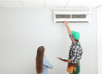 Photo of Male technician speaking with woman about air conditioner indoors