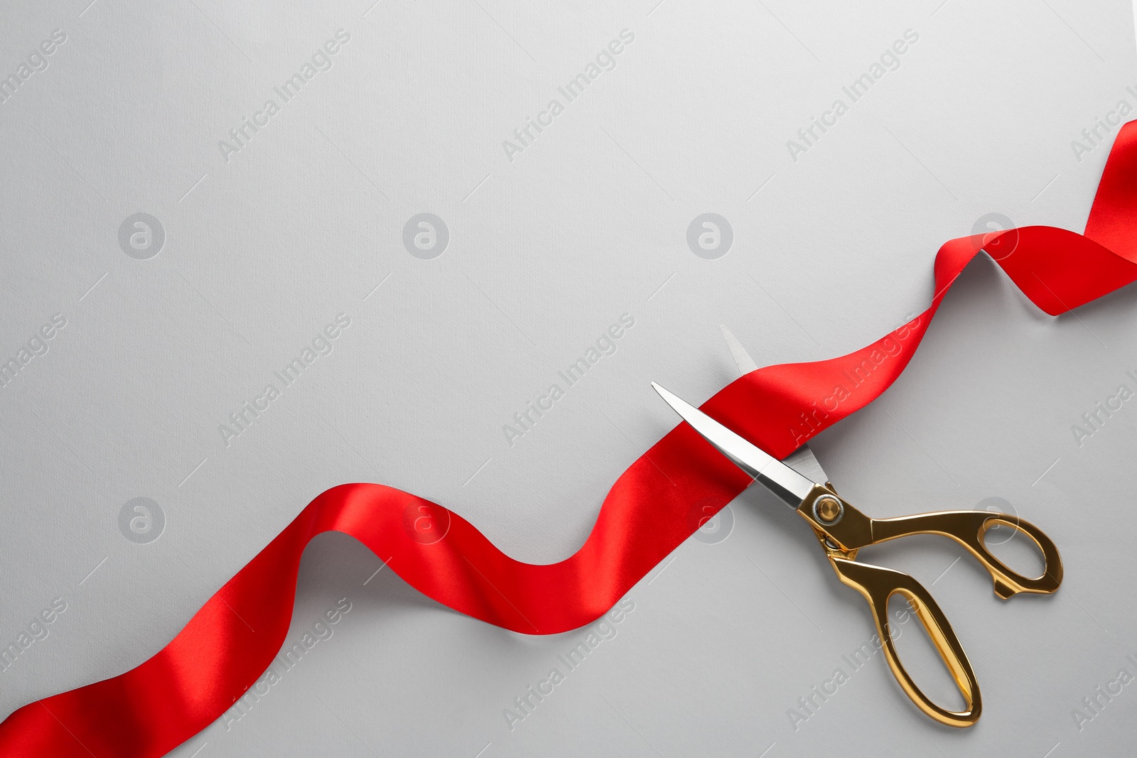 Photo of Red ribbon and scissors on light grey background, top view. Space for text