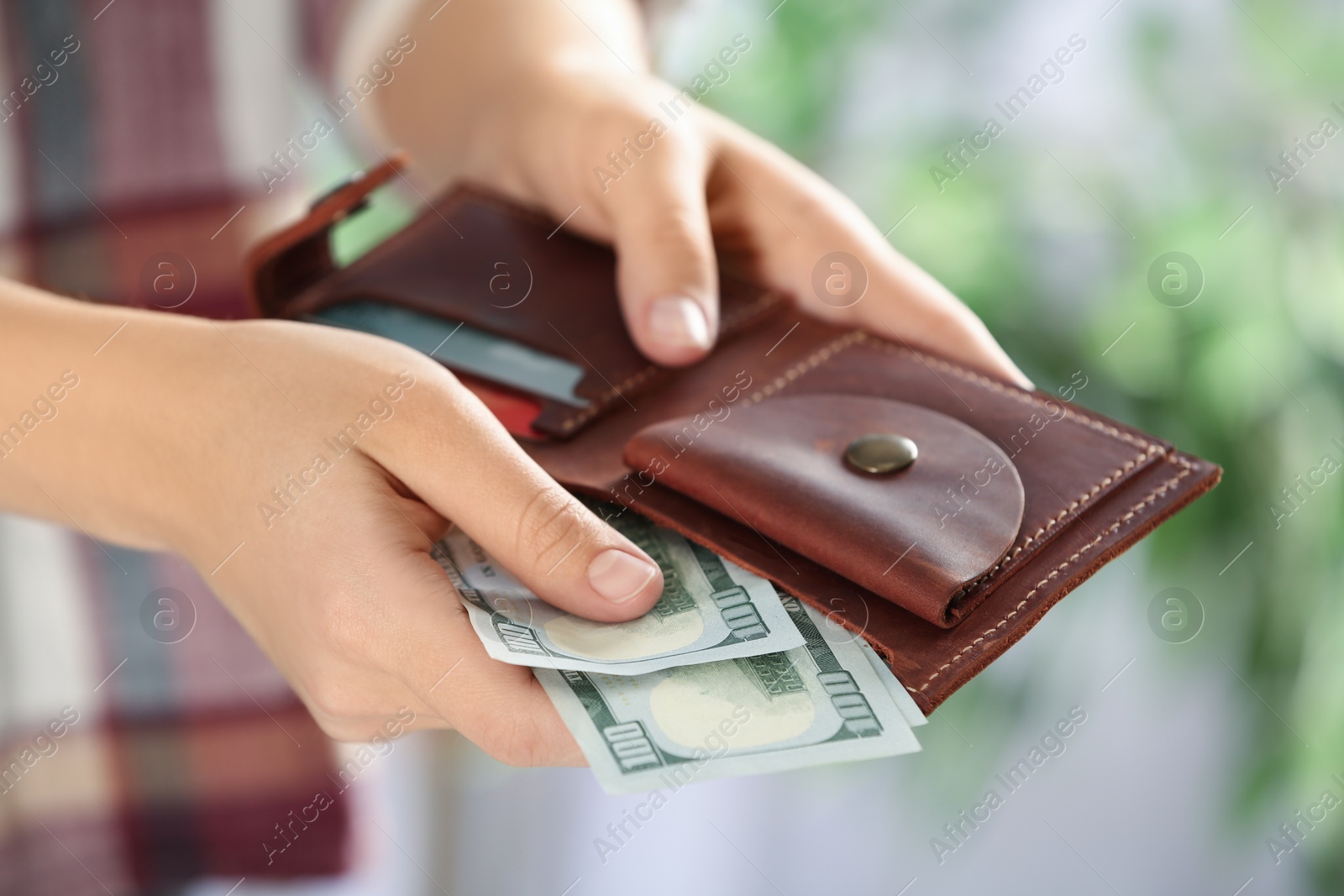 Photo of Woman putting money into wallet on blurred background, closeup