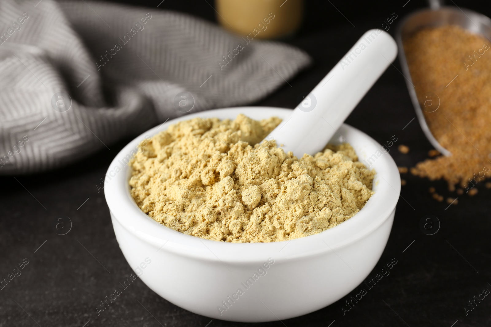 Photo of Mortar with mustard powder on black table, closeup