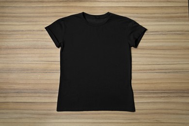 Stylish black T-shirt on wooden table, top view