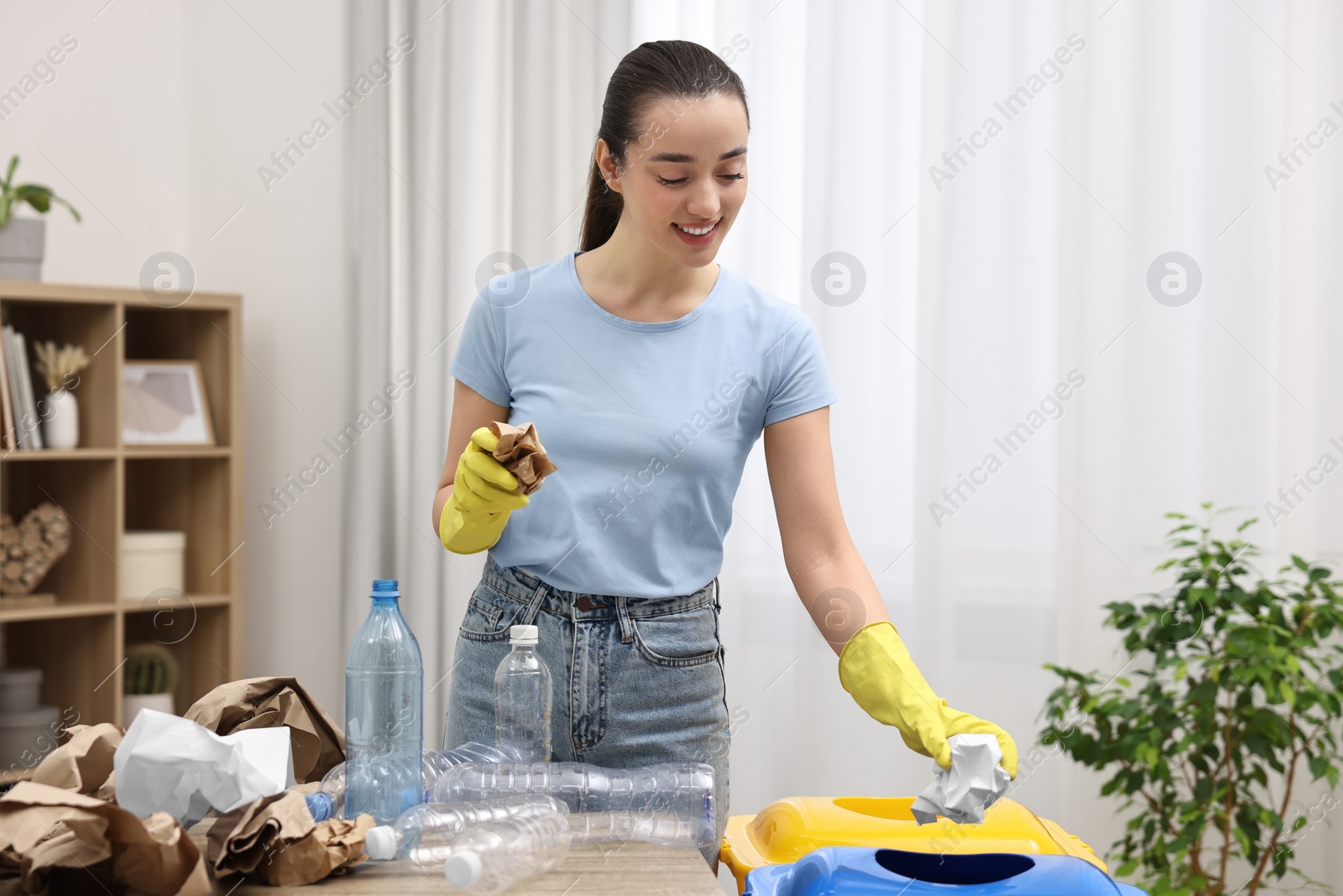 Photo of Garbage sorting. Smiling woman throwing crumpled paper into trash bin in room