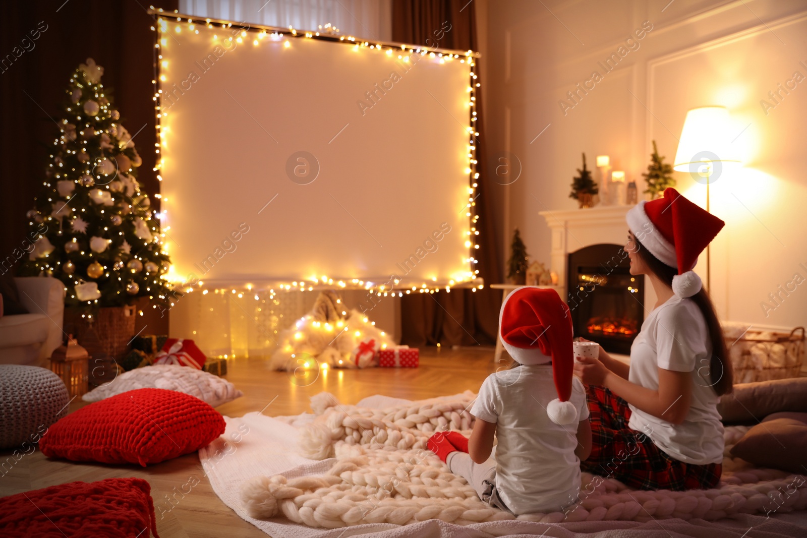 Photo of Mother and daughter watching movie using video projector at home. Cozy Christmas atmosphere