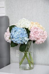 Beautiful hydrangea flowers in vase on white bedside table indoors