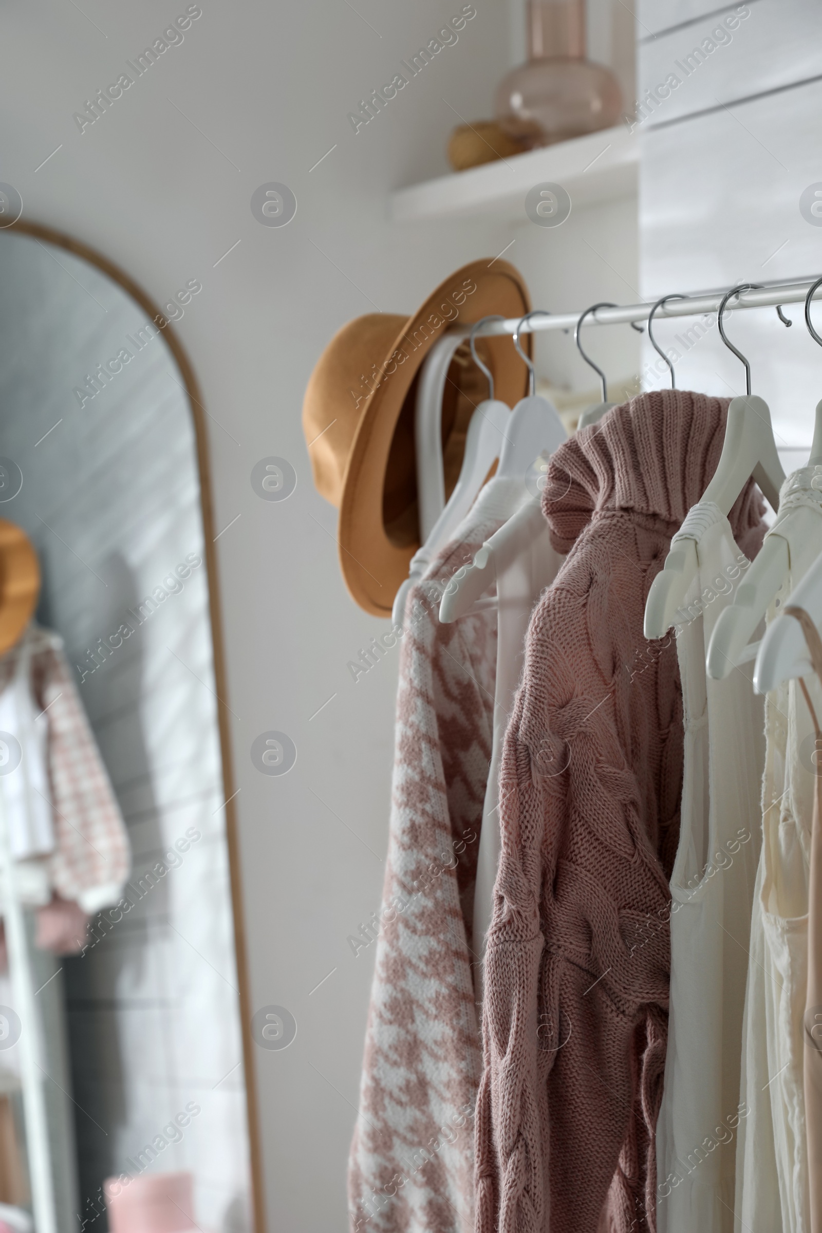 Photo of Rack with different stylish clothes and hat near mirror in dressing room
